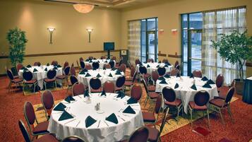 A conference room with multiple tables and chairs, arranged in a circular pattern, with a carpeted floor and a large window providing natural light.