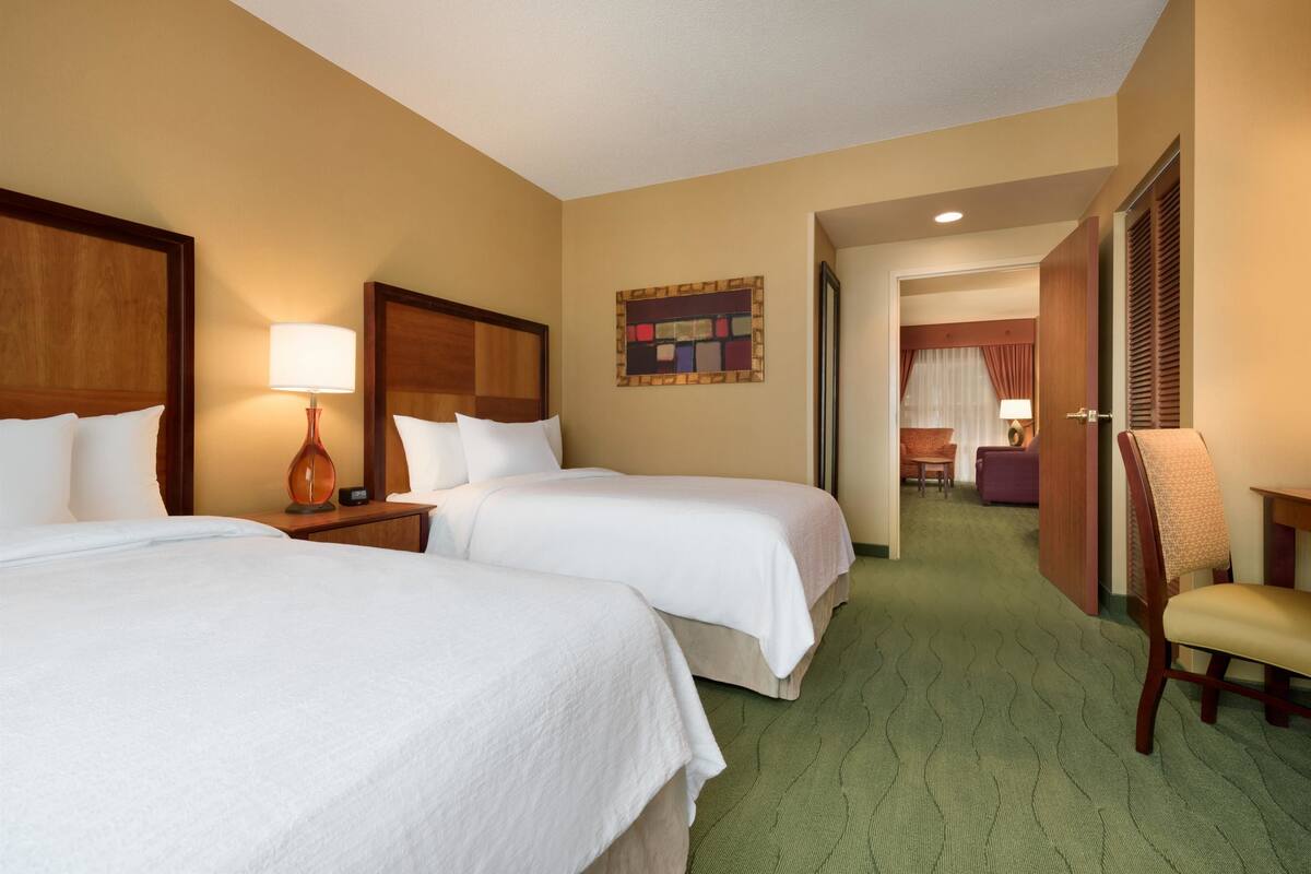 Ein Hotelzimmer mit zwei Betten, einem Sessel, einem Schreibtisch und einer Tür zu einem Badezimmer.