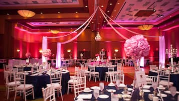 Un salón de banquetes con mesas redondas, sillas blancas y candelabros.