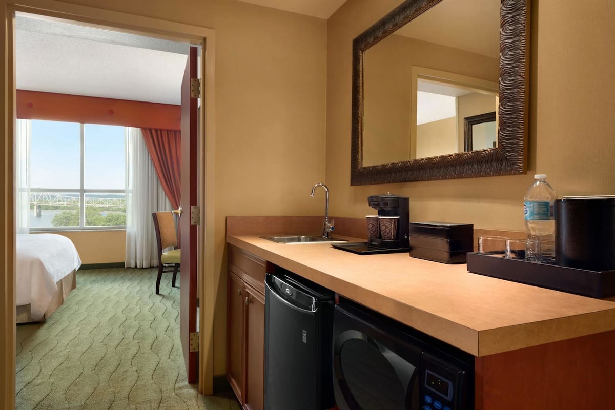 Une chambre d’hôtel avec une kitchenette, un lit, une vue sur un pont et un grand miroir.