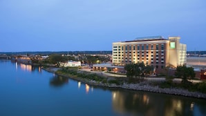 A large hotel with a modern design, situated by a calm body of water, likely offering scenic views and a tranquil environment. - Embassy Suites by Hilton E Peoria Riverfront Conf Center (East Peoria)