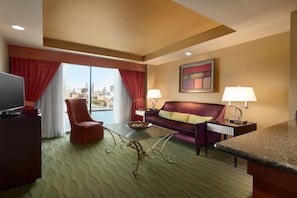 Een hotelkamer met een bank, fauteuil, televisie en uitzicht op de stad.