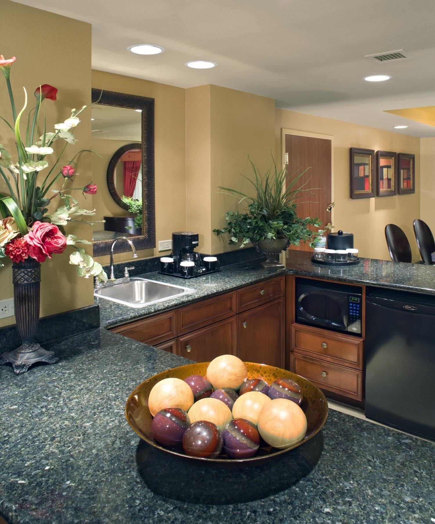 A kitchen with granite countertops, a coffee maker, a sink, and a bowl of fruit.