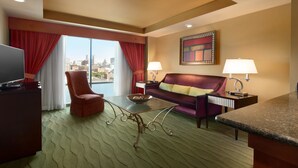 A hotel room with a large window, a sofa, a chair, a small table, a TV, and two lamps. - Embassy Suites by Hilton E Peoria Riverfront Conf Center (East Peoria)