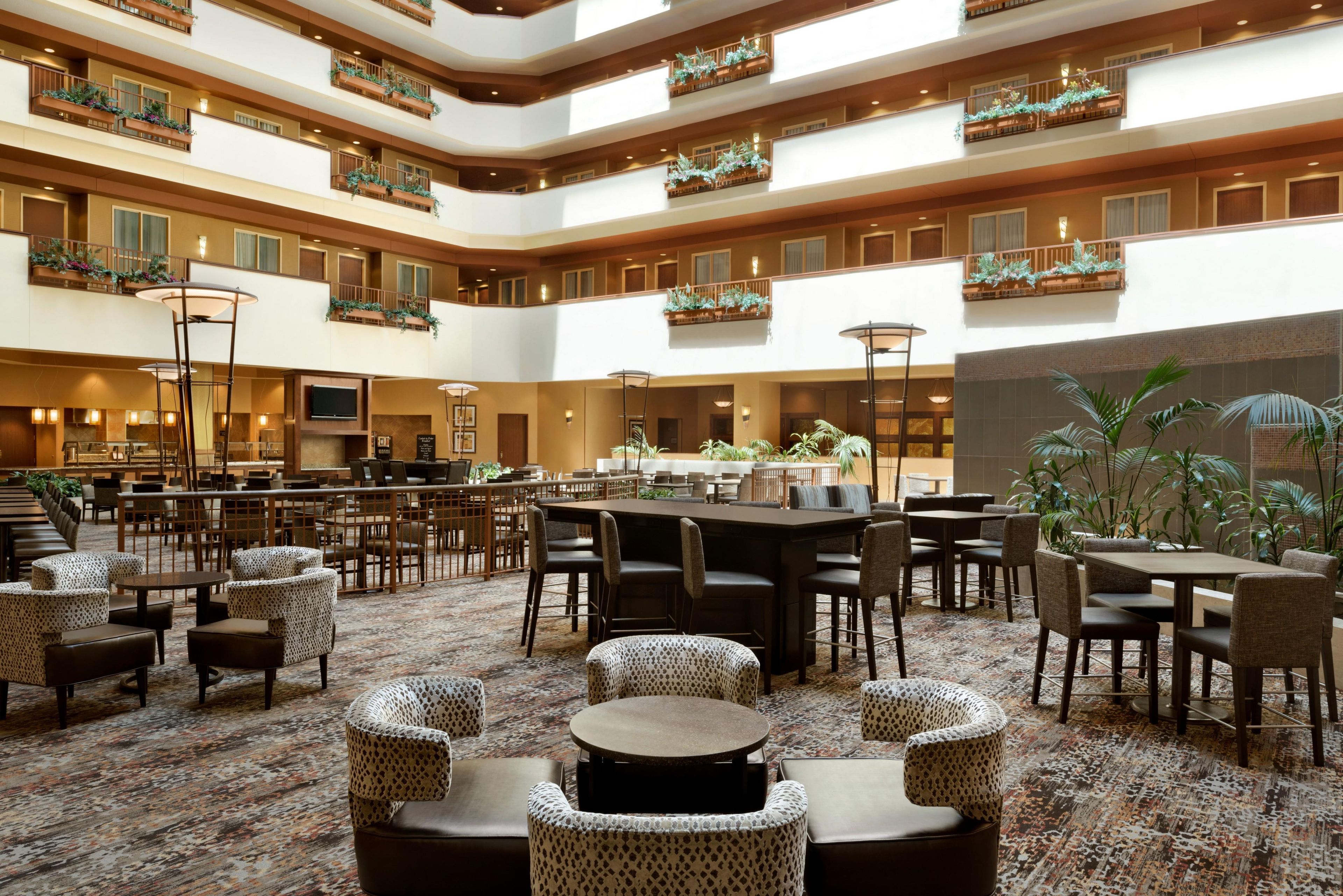 A multi-level hotel lobby with a central dining area, multiple seating arrangements, and decorative plants.