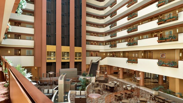 A multi-level hotel atrium with a central staircase, multiple balconies, and a variety of seating areas. - Embassy Suites by Hilton E Peoria Riverfront Conf Center (East Peoria)