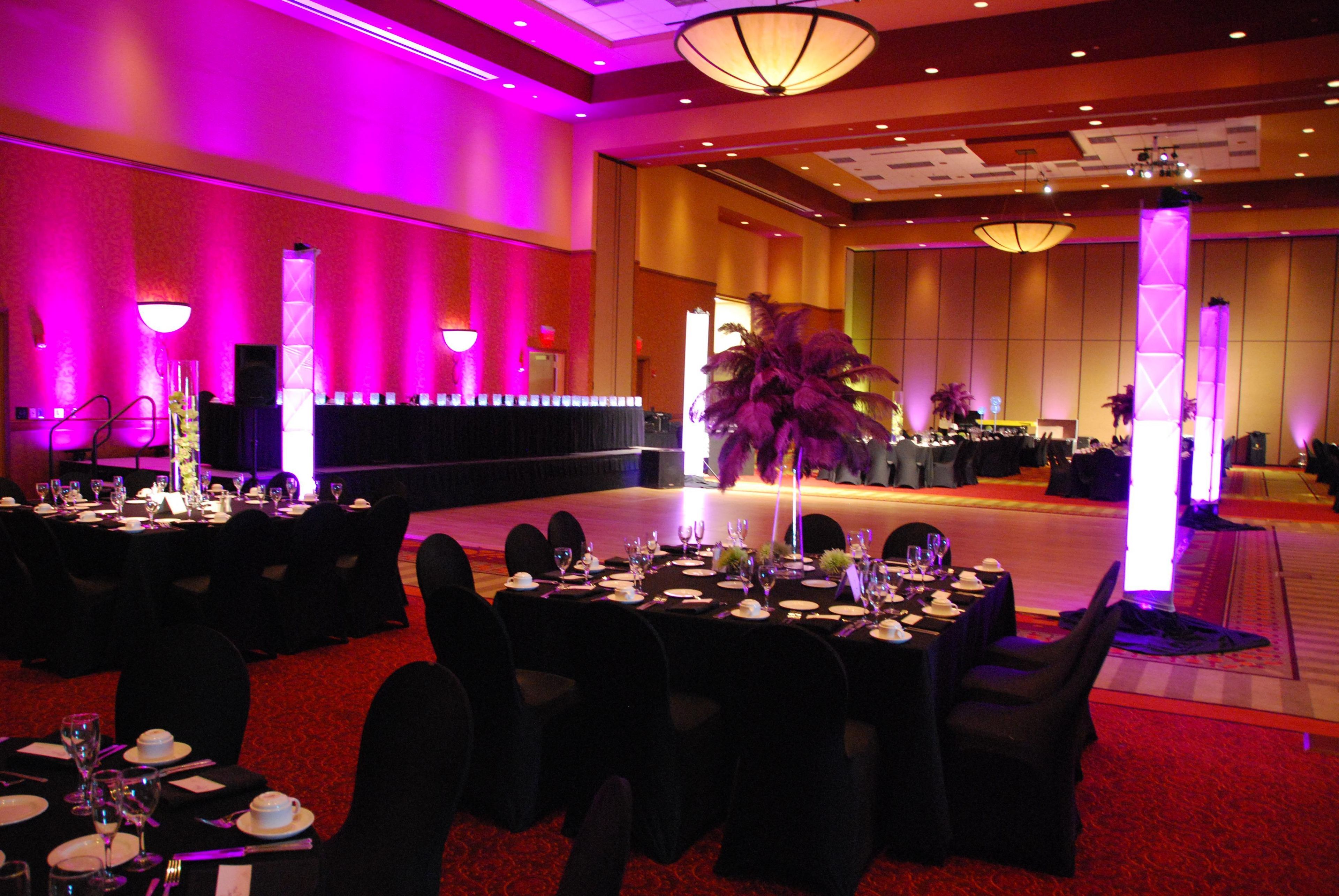 A banquet hall with tables set for a formal event, featuring a central floral arrangement and a stage area.
