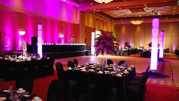 A banquet hall with tables set for a formal event, featuring a central floral arrangement and a stage area.