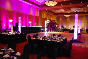A banquet hall with tables set for a formal event, featuring a central floral arrangement and a stage area.