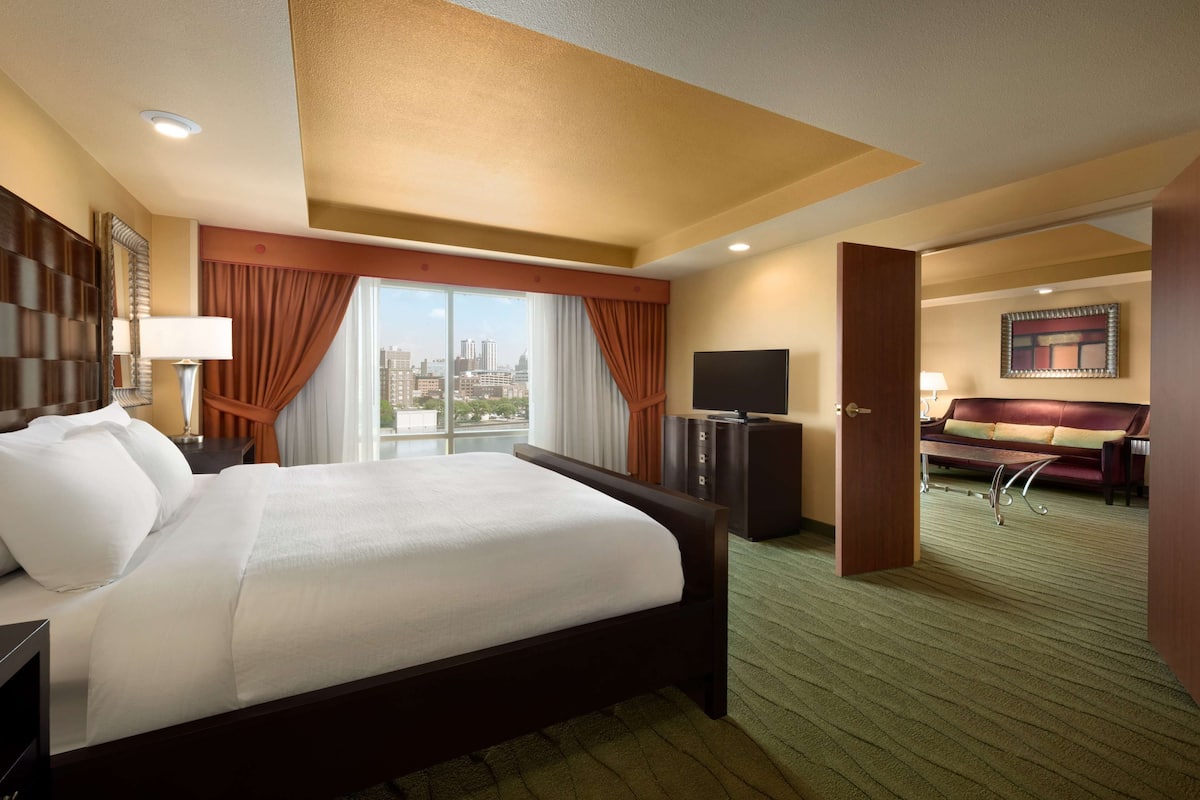 Ein Hotelzimmer mit einem großen Bett, einem Fernseher, einem Schreibtisch und Blick auf die Stadt.