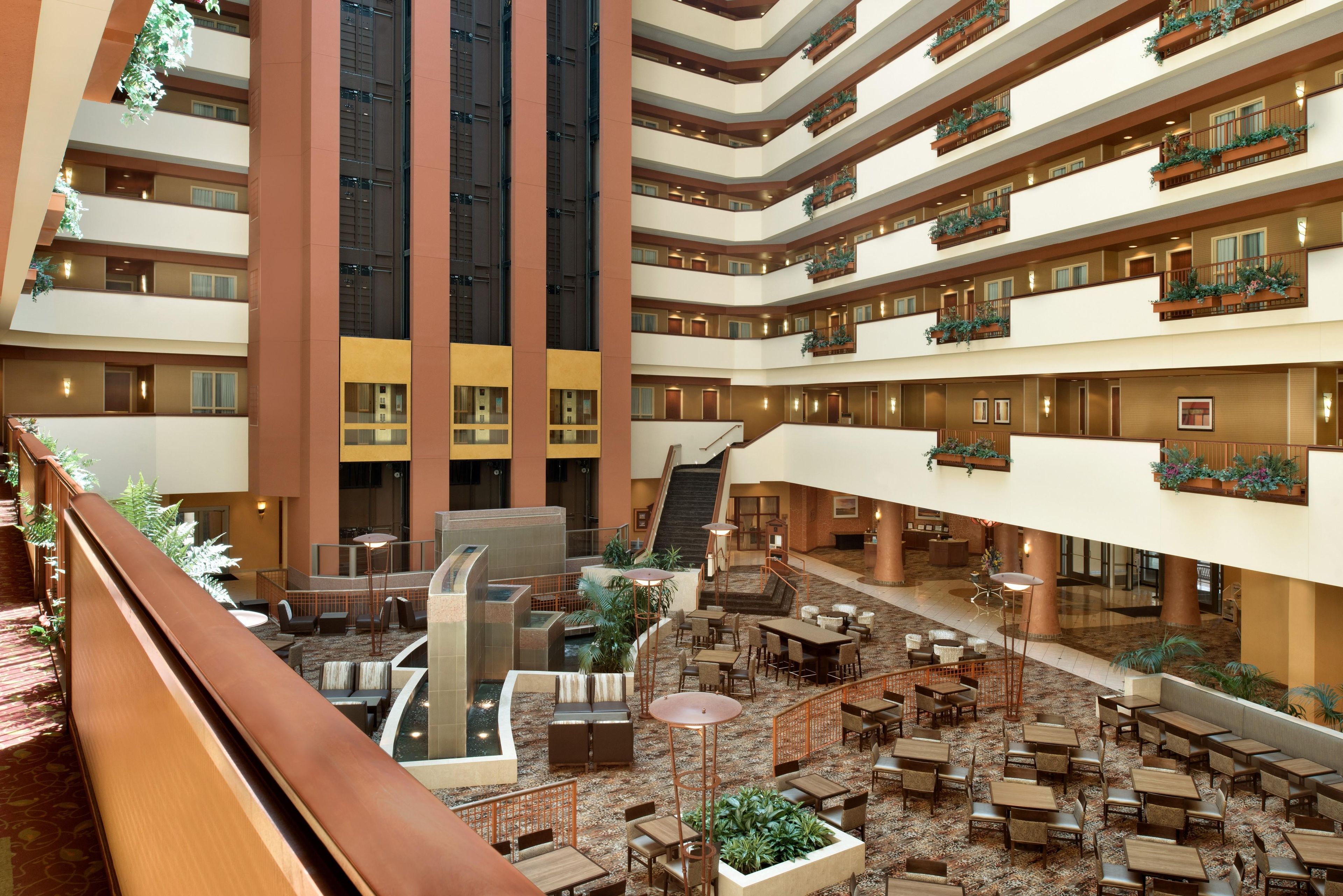 A multi-level hotel atrium with a central staircase, outdoor seating areas, and balconies with greenery.