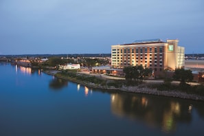 Un hotel con un edificio grande, un río al frente y un puente al fondo.