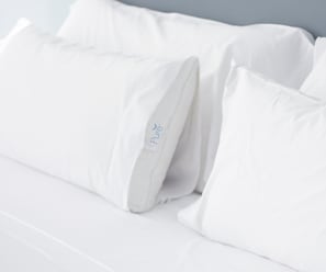Una cama con ropa de cama y almohadas blancas, una de ellas con el logo 'Pure'.