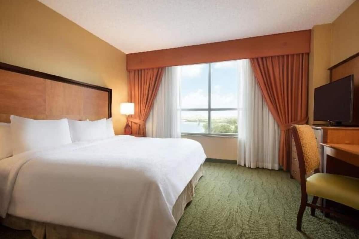 Ein Hotelzimmer mit Bett, Schreibtisch, Stuhl, Fernseher und einem Fenster mit Vorhängen.