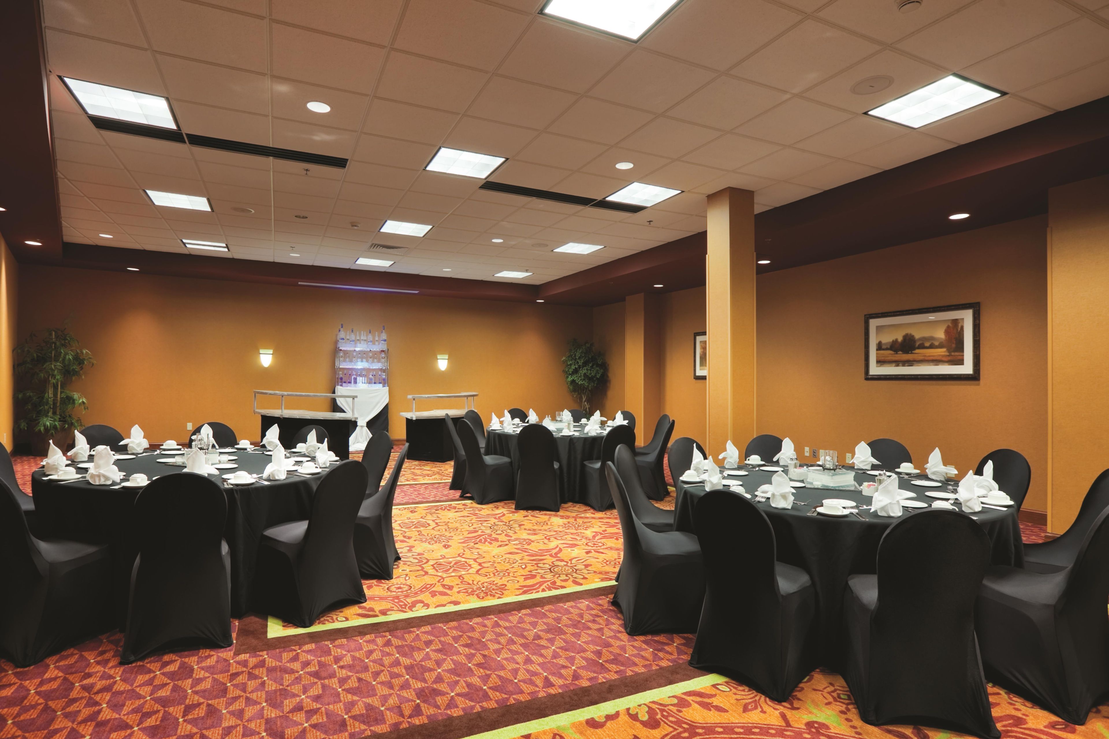 Un salón de conferencias con mesas redondas, sillas negras y una alfombra estampada.