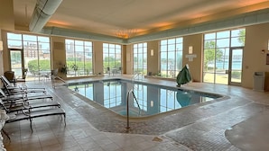 An indoor swimming pool with clear views of the outside, surrounded by benches and tables. - Embassy Suites by Hilton E Peoria Riverfront Conf Center (East Peoria)