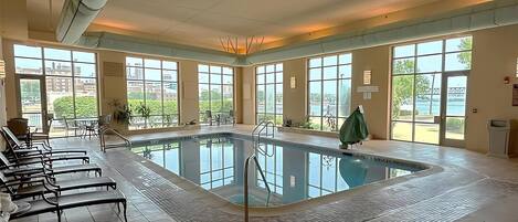 Une piscine intérieure offrant une vue dégagée sur l’extérieur, entourée de bancs et de tables.