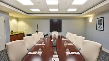 Un salón de conferencias con una larga mesa, ocho sillas y una pantalla para proyector en la pared.