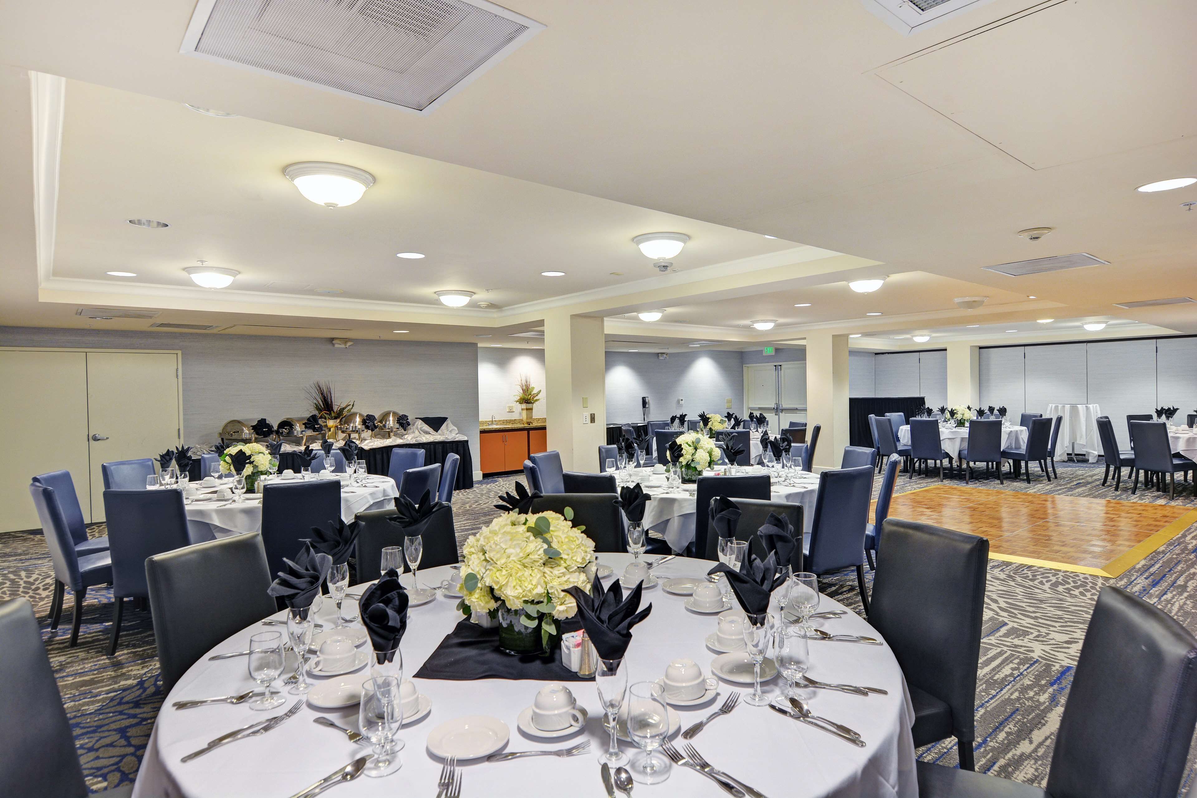 A banquet hall with round tables set for dining, featuring white tablecloths, black napkins, and floral centerpieces.