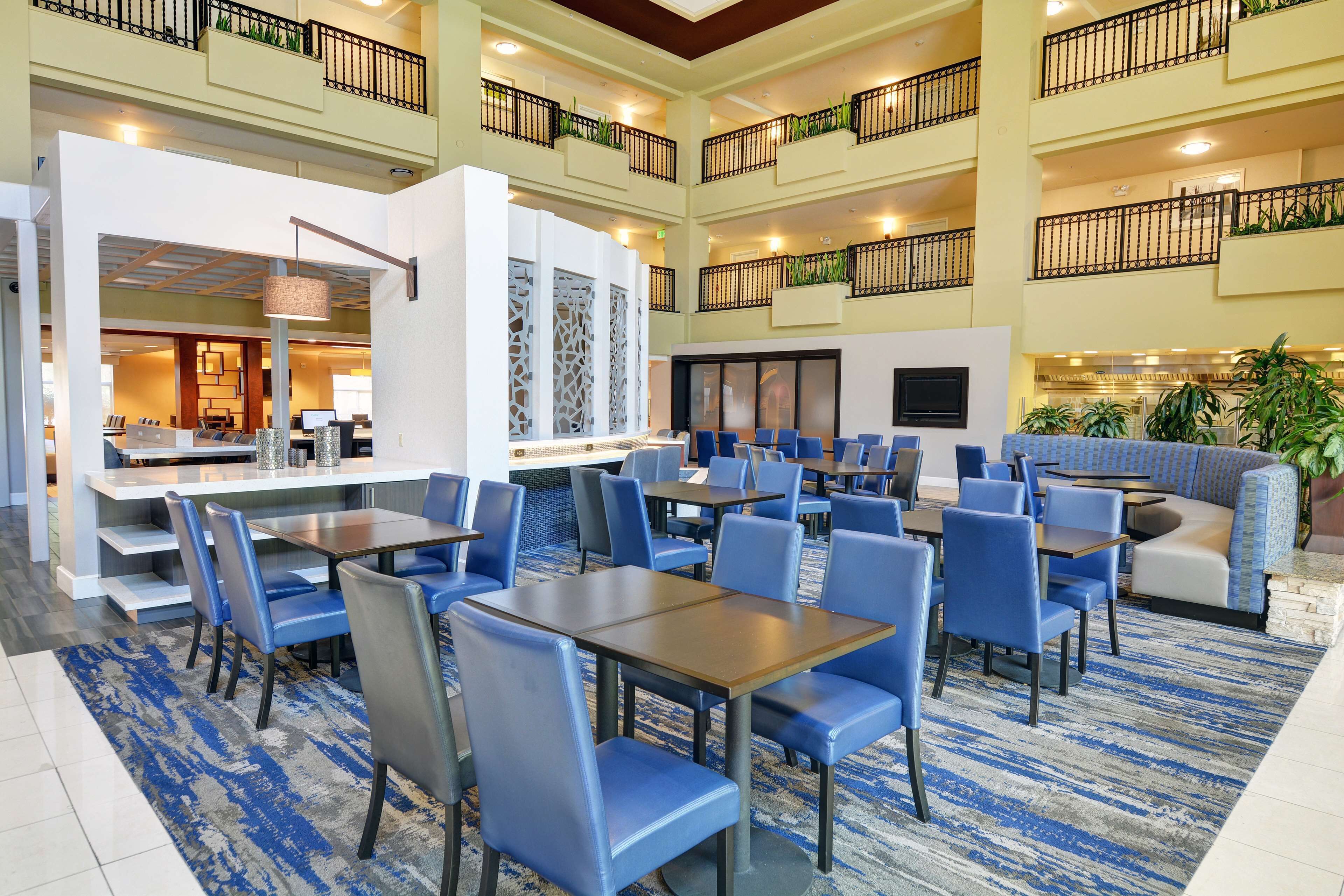 A hotel lobby with multiple dining areas, seating arrangements, and a reception desk.
