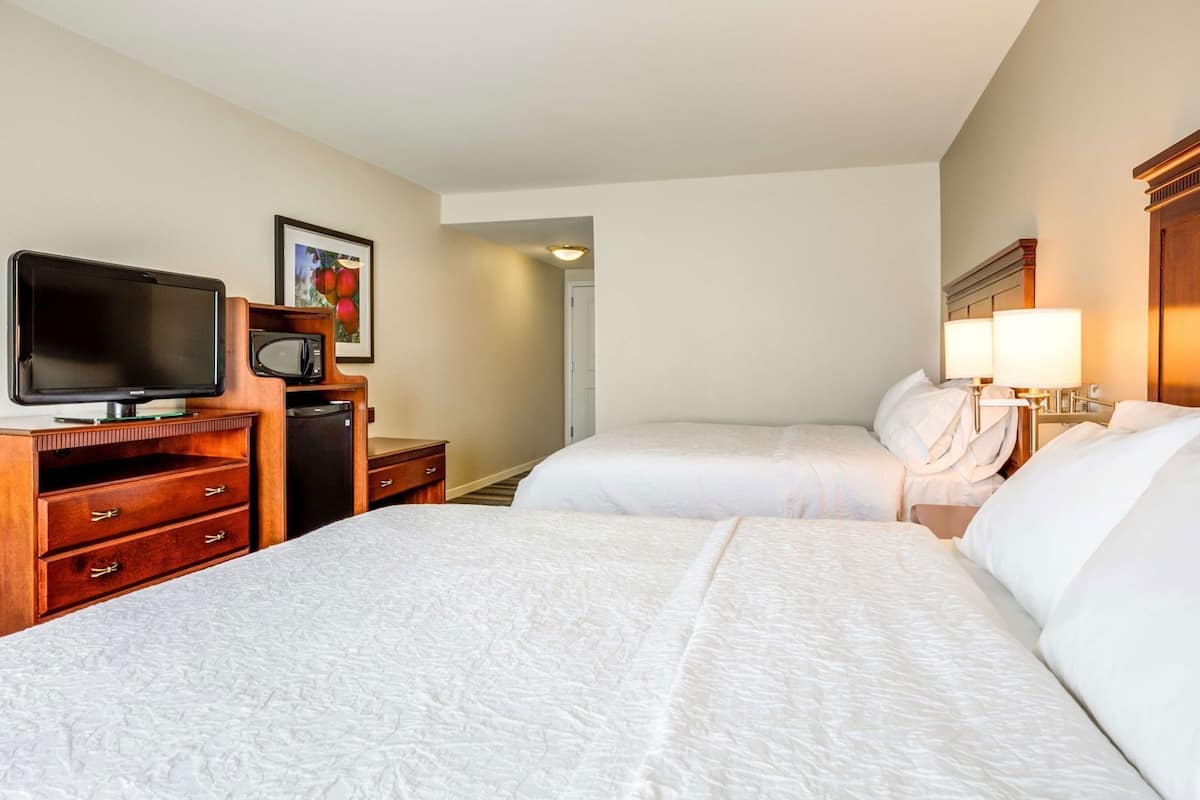 Een hotelkamer met twee bedden, een televisie, een bureau met een computer en een lijst met een ingelijst beeld.