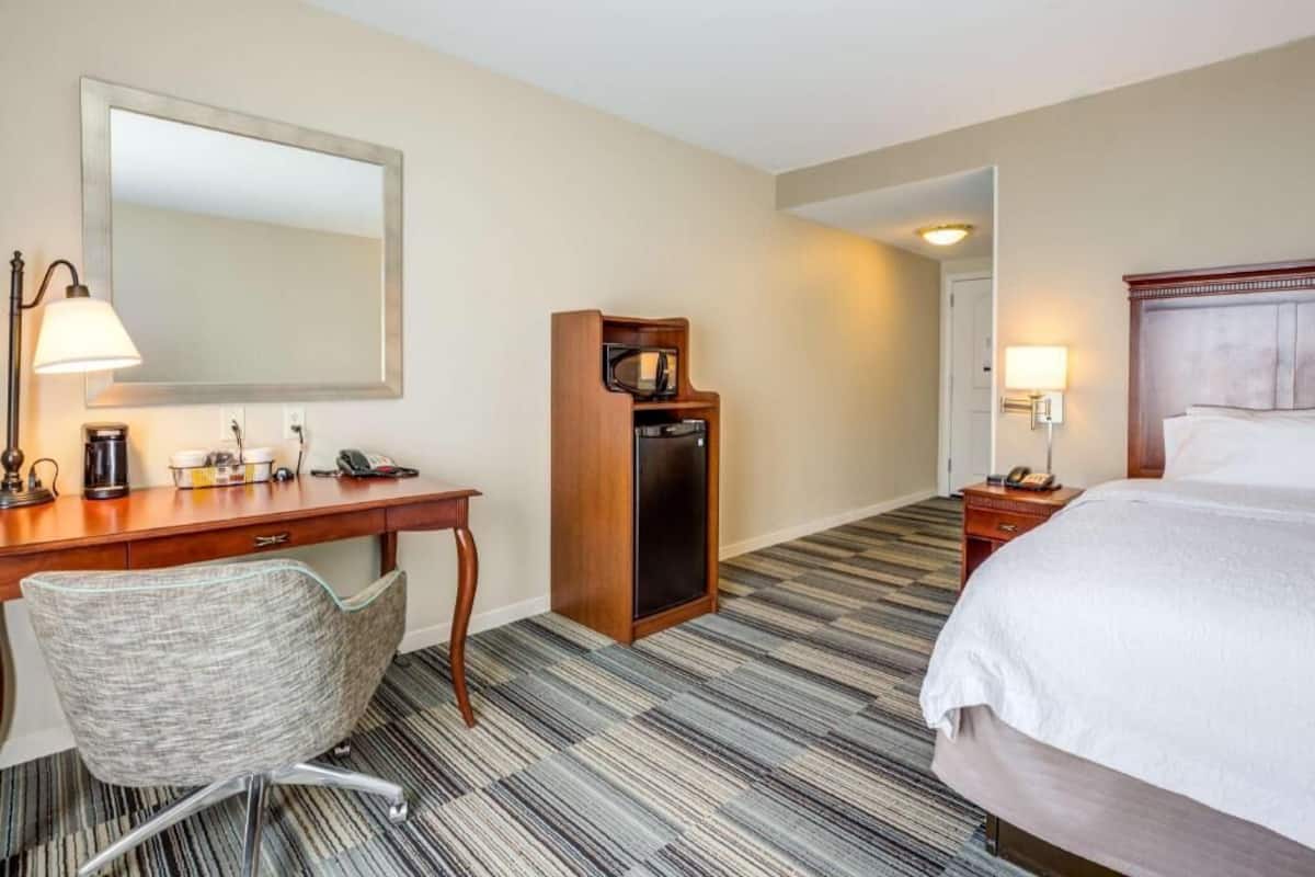 Een hotelkamer met een bed, een bureau met lamp, een stoel, een televisietoestel en een koelkast.