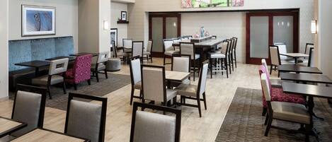 Ein Hotelrestaurant mit mehreren Tischen und Stühlen, einer zentralen Insellounge und Kunstwerken an den Wänden.