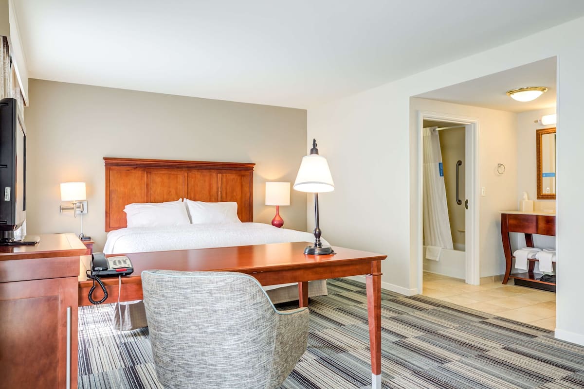 Een hotelkamer met een bed, bedlampen, een bureau met telefoon, een stoel en een badkamer die door een open deur zichtbaar is.