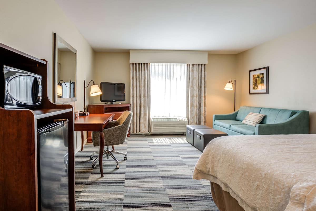 Hotelkamer met een bed, een bureau met stoel, een televisie, een magnetron, een lamp en een raam met gordijnen.