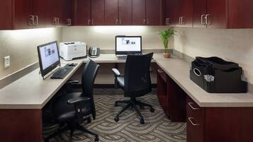 Un espace de bureau moderne comprenant deux bureaux, des ordinateurs, une imprimante, un téléphone, une plante en pot et une mallette noire.