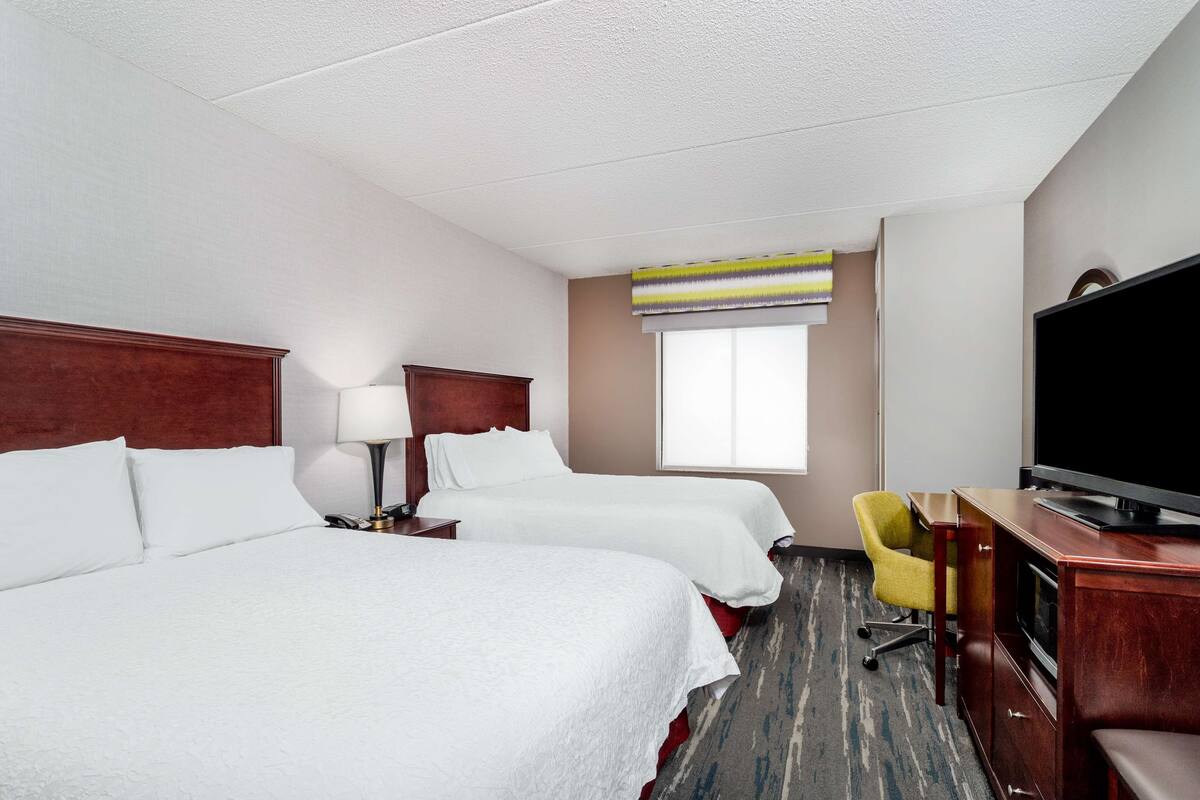 A hotel room with two beds, a TV, a desk, and a chair.