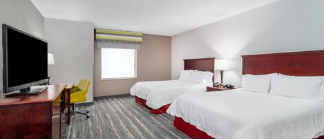 Habitación de hotel con dos camas, un escritorio con televisor, una silla y una ventana con persianas.