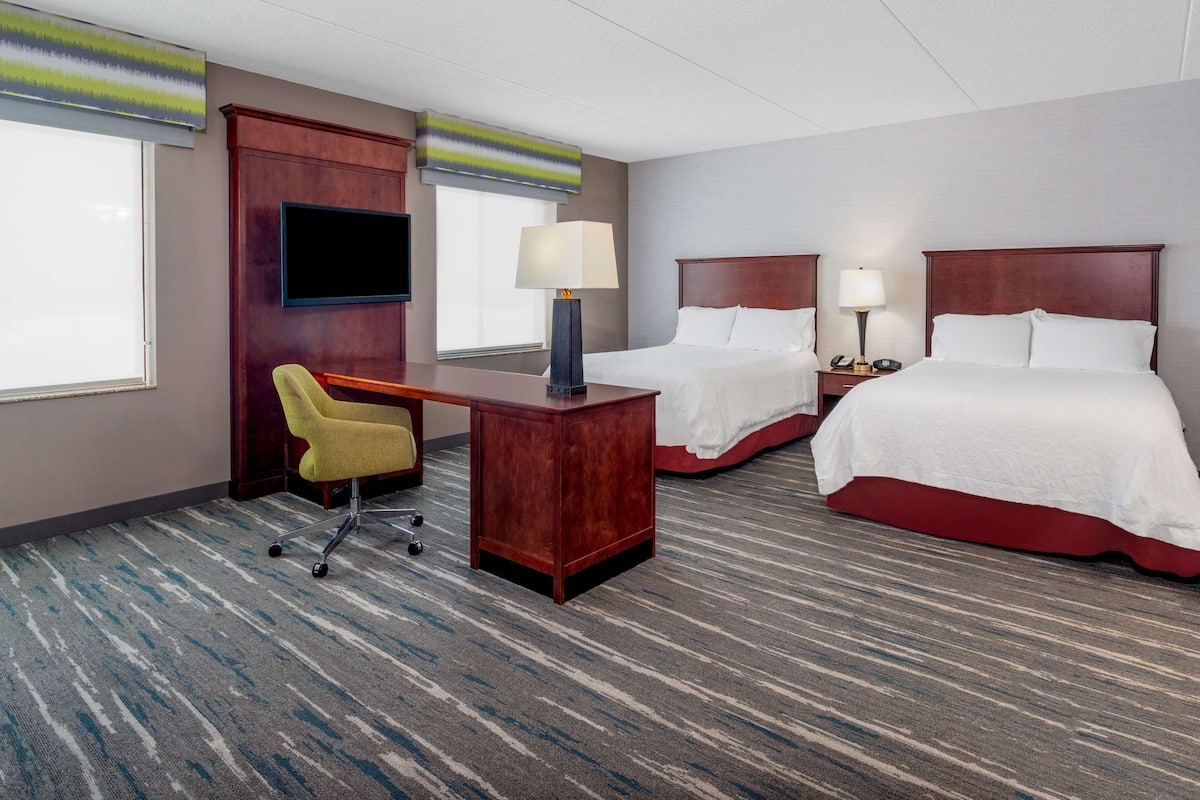 A hotel room with a desk, two beds, a TV, and a chair.