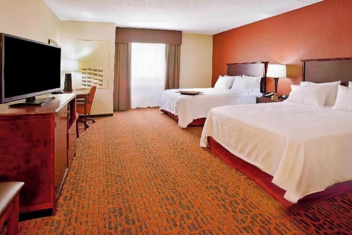 A hotel room with two beds, a TV, a desk, and a chair.