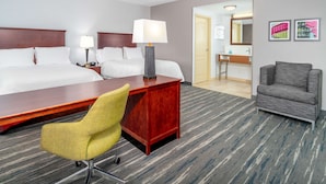 Een hotelkamer met een groot bed, een bureau met een lamp, een stoel en een fauteuil. In de achtergrond is een badkamer zichtbaar.