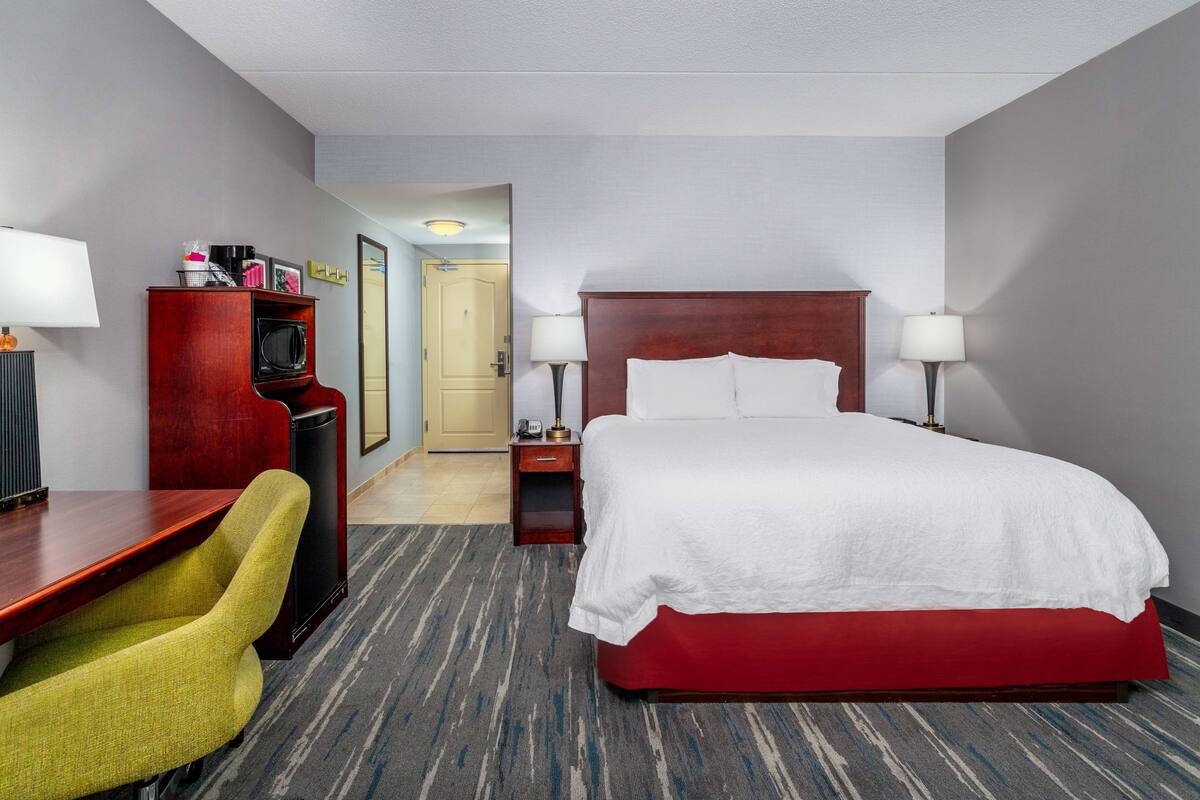 A hotel room with a large bed, a desk with a chair, a microwave, and a TV.