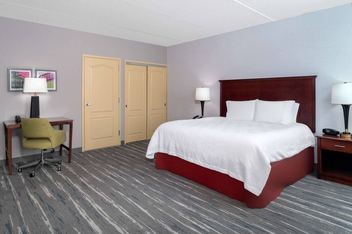A hotel room with a large bed, two doors, a desk with a chair, and two bedside lamps.