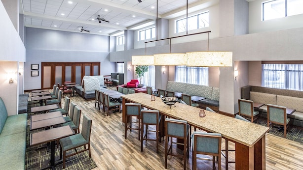 Een ruime hotellobby met verschillende zithoeken, waaronder een lange gemeenschappelijke tafel en diverse banken en stoelen.