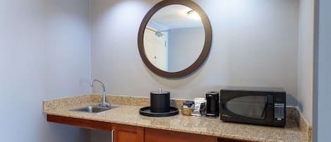 A compact kitchenette with a granite countertop, a sink, a coffee maker, a microwave, and a compact dishwasher.