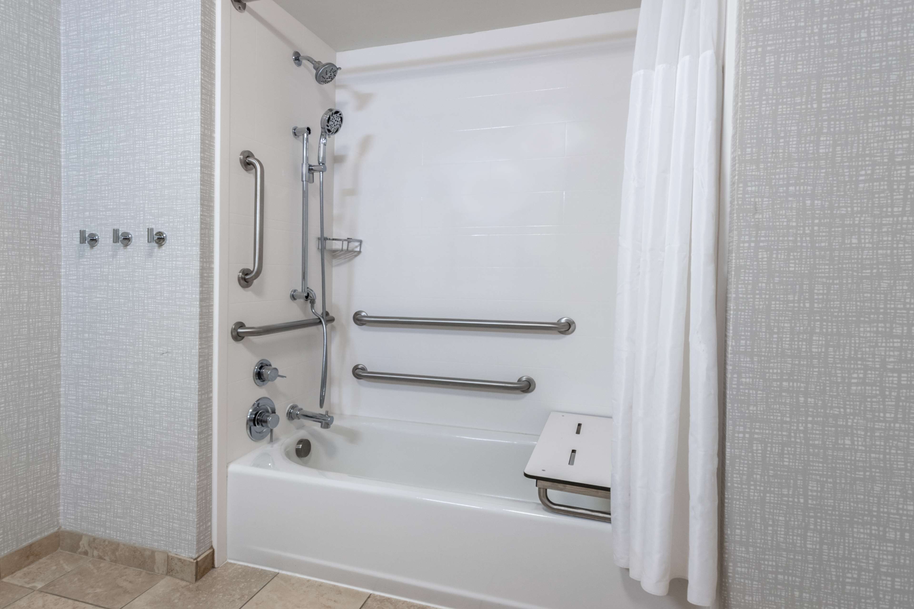 A white bathtub with grab bars, a showerhead, and a handheld shower attachment.