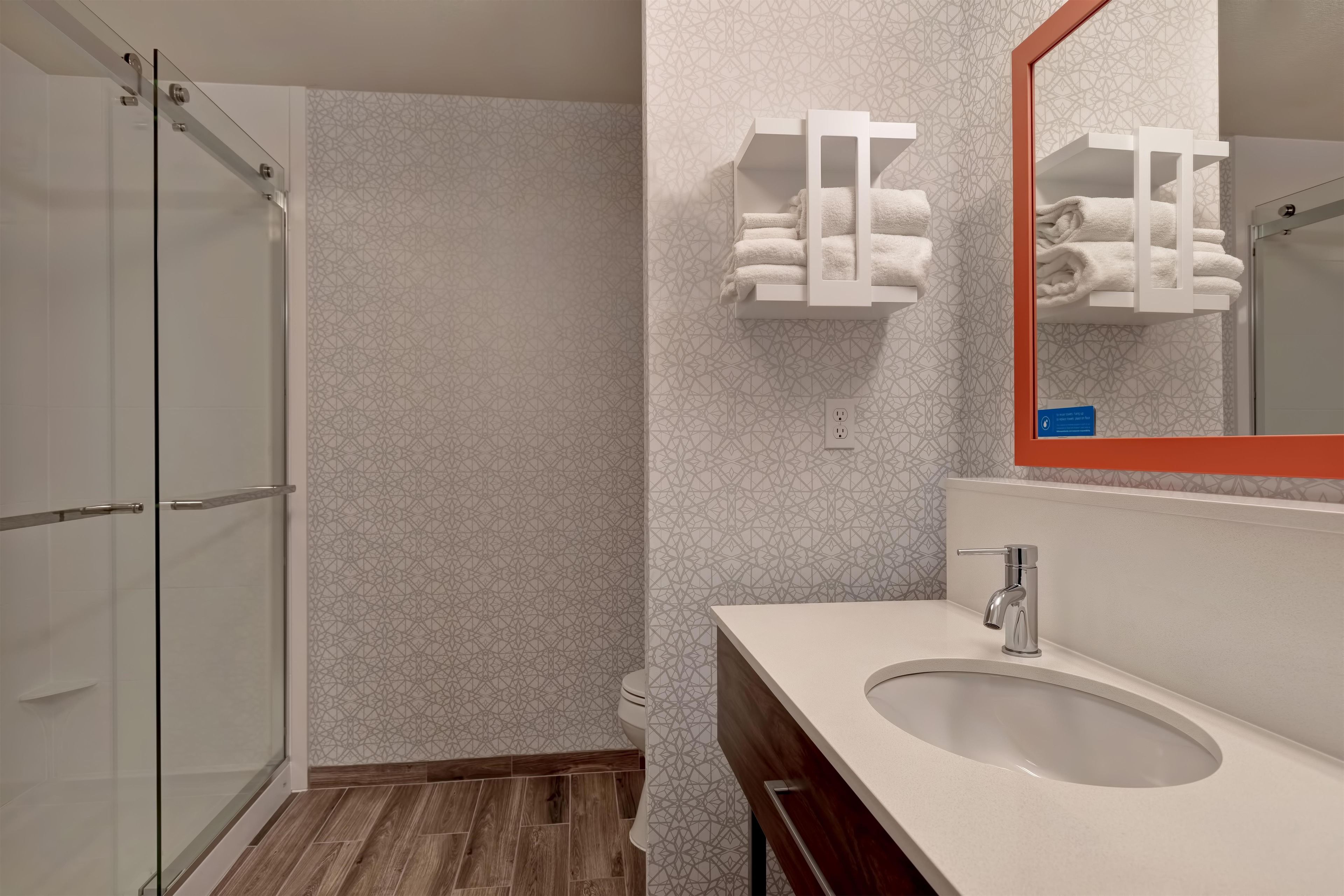 A bathroom with a glass shower enclosure, a sink with a mirror, and a towel rack.