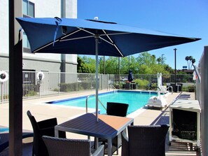 Un área junto a la piscina con mesa y sillas, una sombrilla grande y piscina cercada.