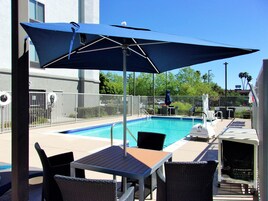 A poolside area with a table and chairs, a large umbrella, and a fenced pool.