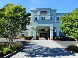 A Hampton Inn & Suites building with a modern facade, large entrance, and surrounding landscaping.