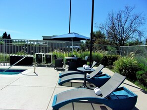 A poolside area with lounge chairs and a table, surrounded by a fence and greenery. - Hampton Inn & Suites Rohnert Park - Sonoma County (Rohnert Park)