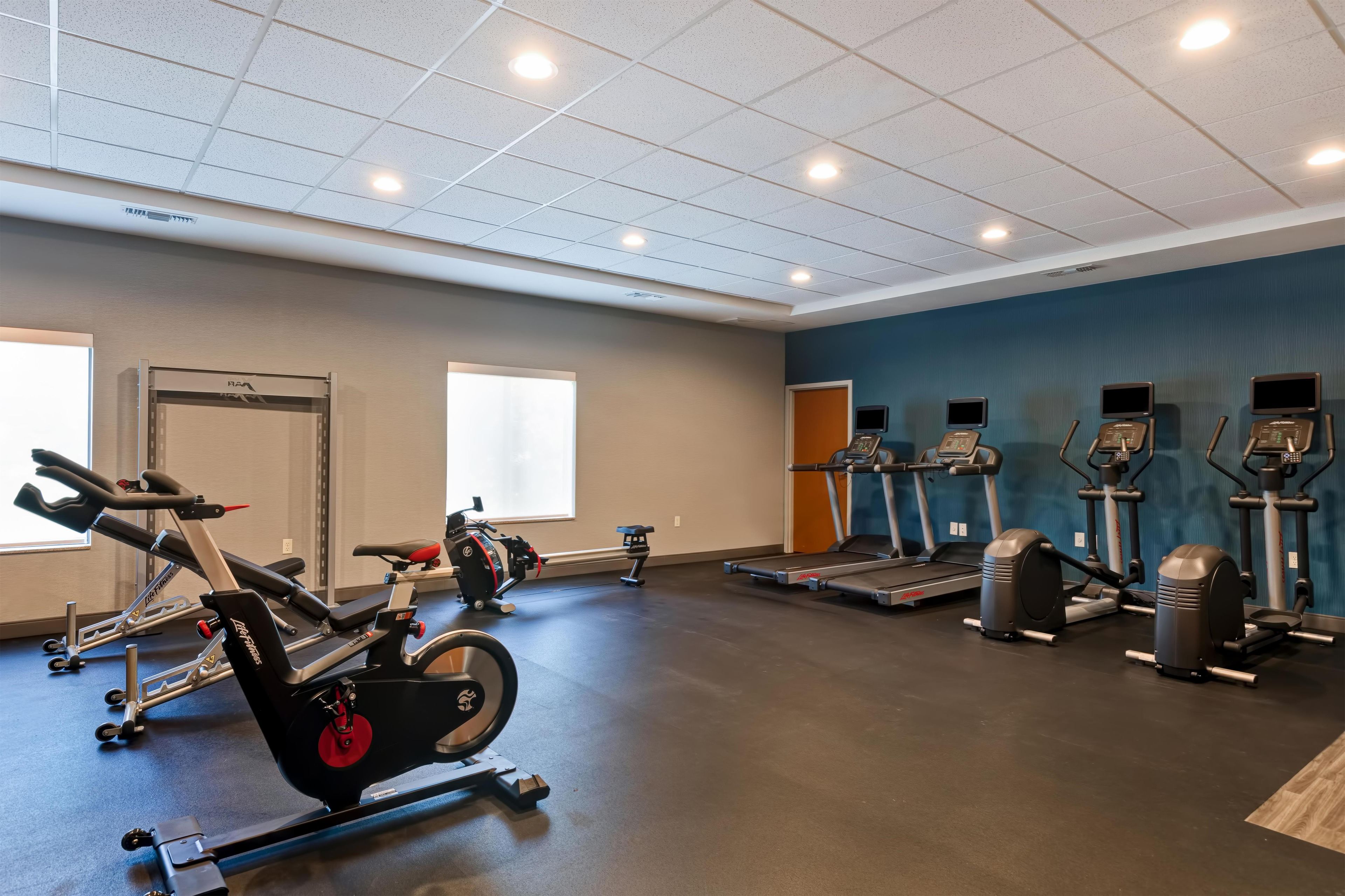 Une salle de sport équipée de divers appareils d’exercice, notamment des tapis de course et des vélos d’appartement, et dotée d’une grande fenêtre qui laisse entrer la lumière naturelle.