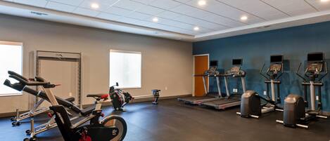 Une salle de sport équipée de divers appareils d’exercice, notamment des tapis de course et des vélos d’appartement, et dotée d’une grande fenêtre qui laisse entrer la lumière naturelle.