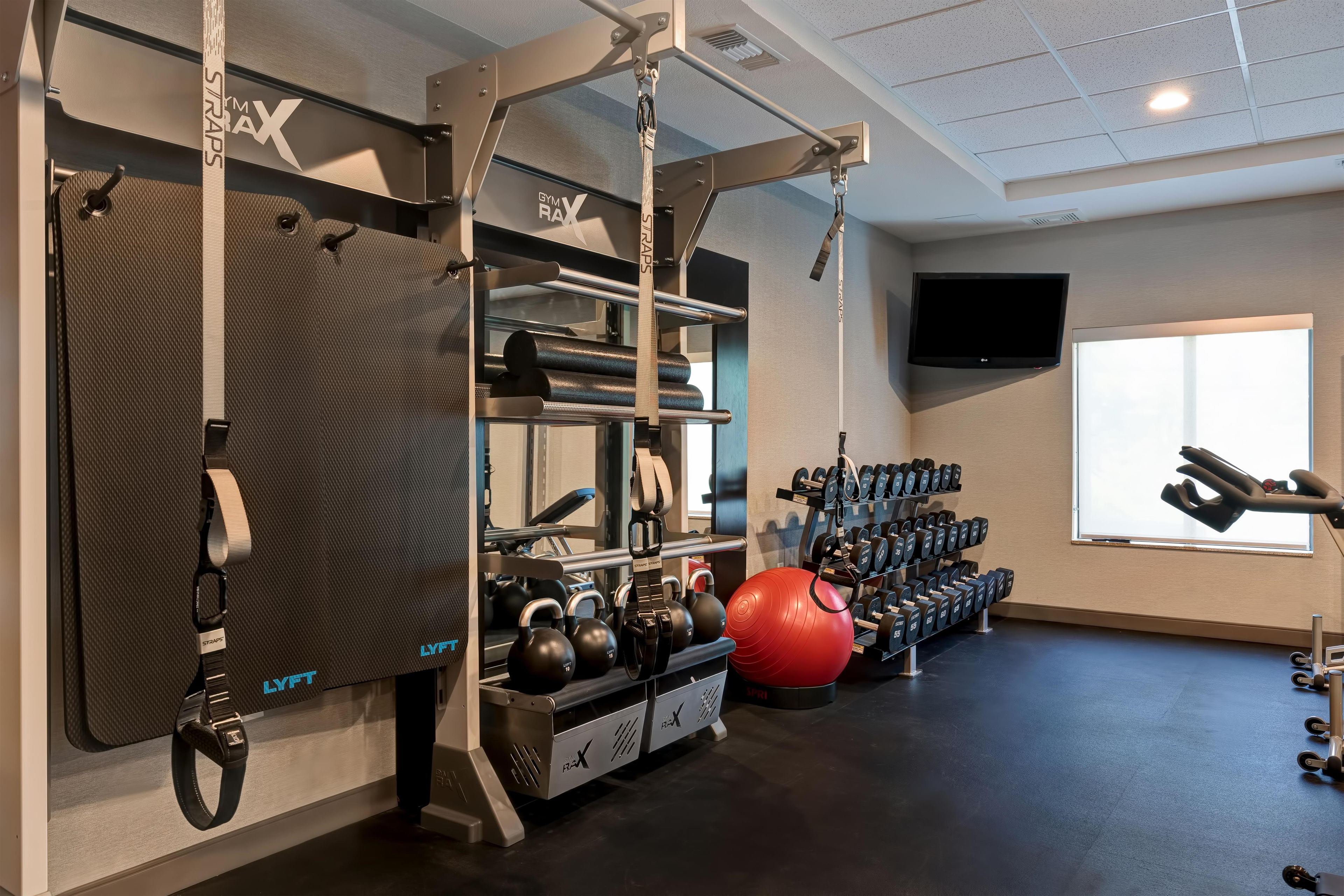 Une salle de sport équipée de matériel de musculation, de kettlebells et d’un ballon d’exercice rouge.