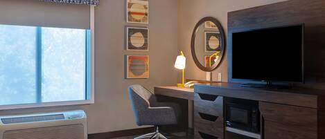 A hotel room with a bed, desk, chair, television, and artwork on the wall.