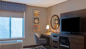Een hotelkamer met een bed, een bureau met stoel, een televisie, een spiegel en kunst aan de muur.